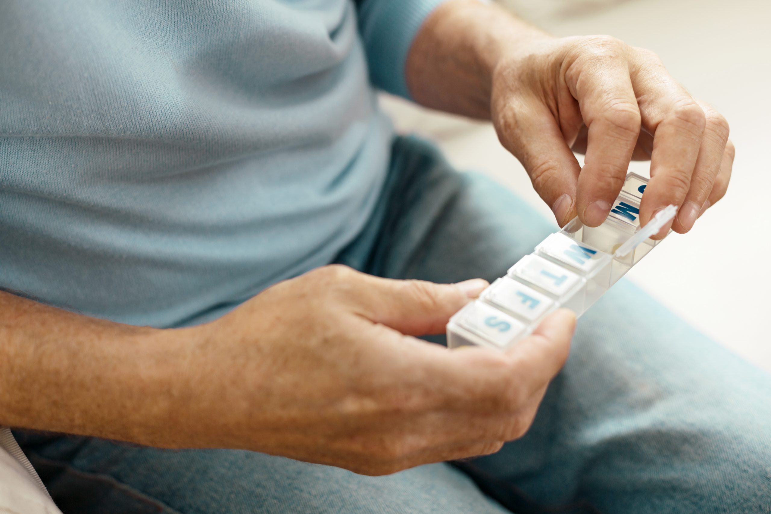 Pill organizer. Close up of a plastic pill container being held by a nice pleasant elderly man while taking medicine