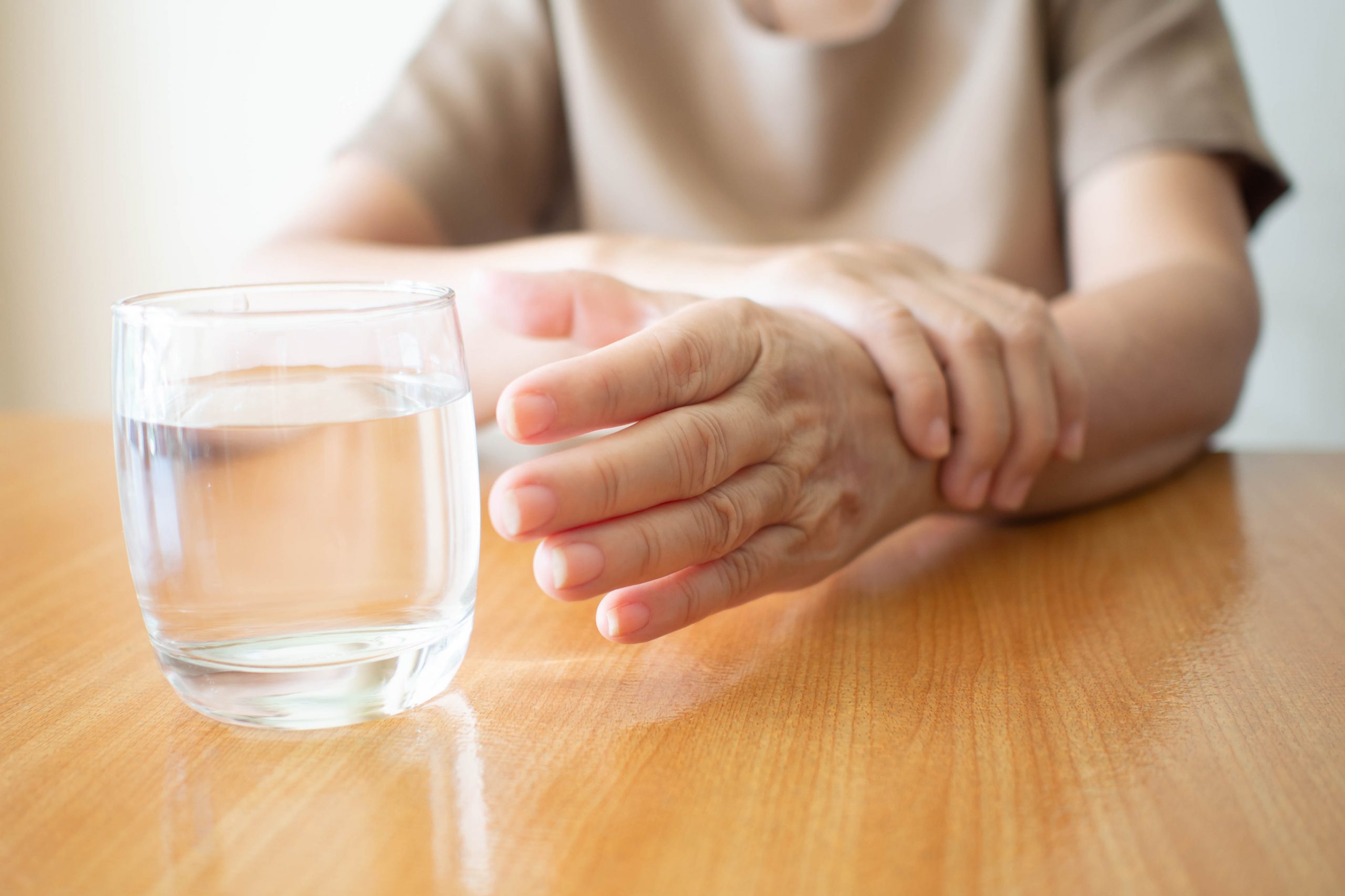 Elderly woman hands w/ tremor symptom reaching out for a glass o