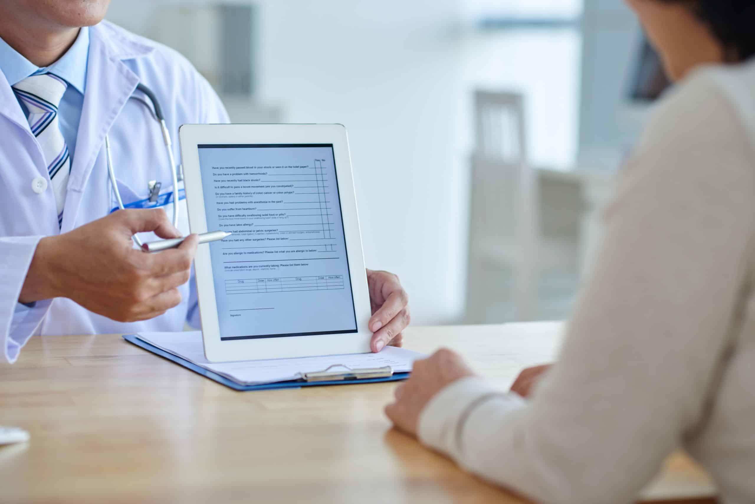 Close-up shot of physician pointing at screen of digital tablet, female patient listening to him with concentration